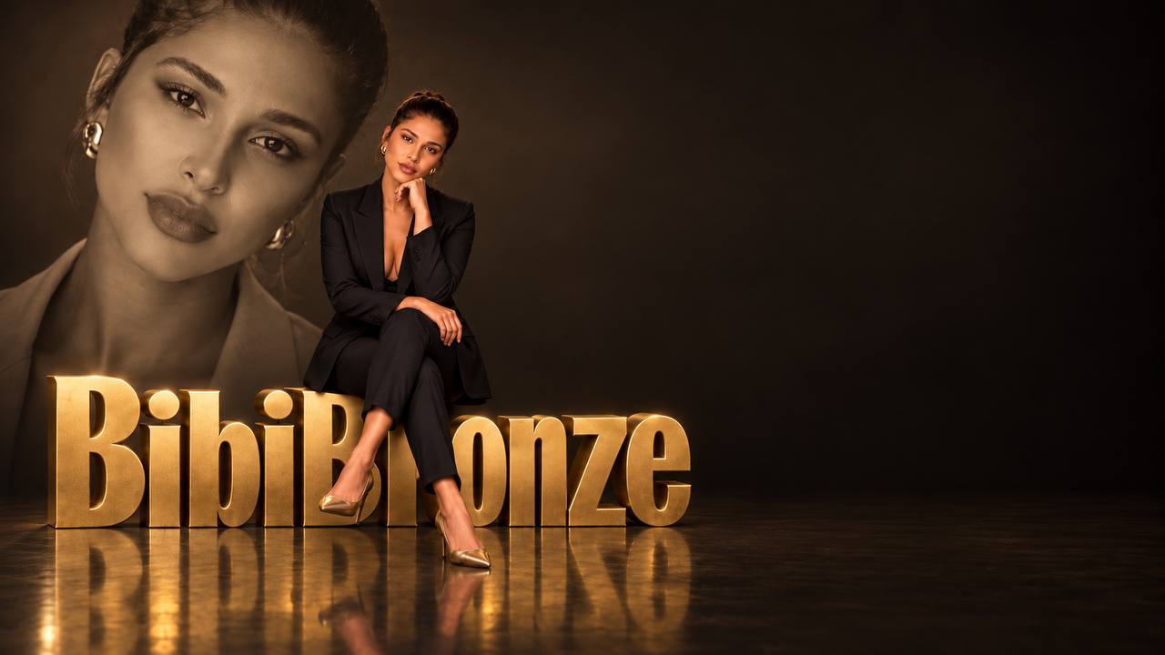 Bibi Bronze sentada em seu cenário dourado